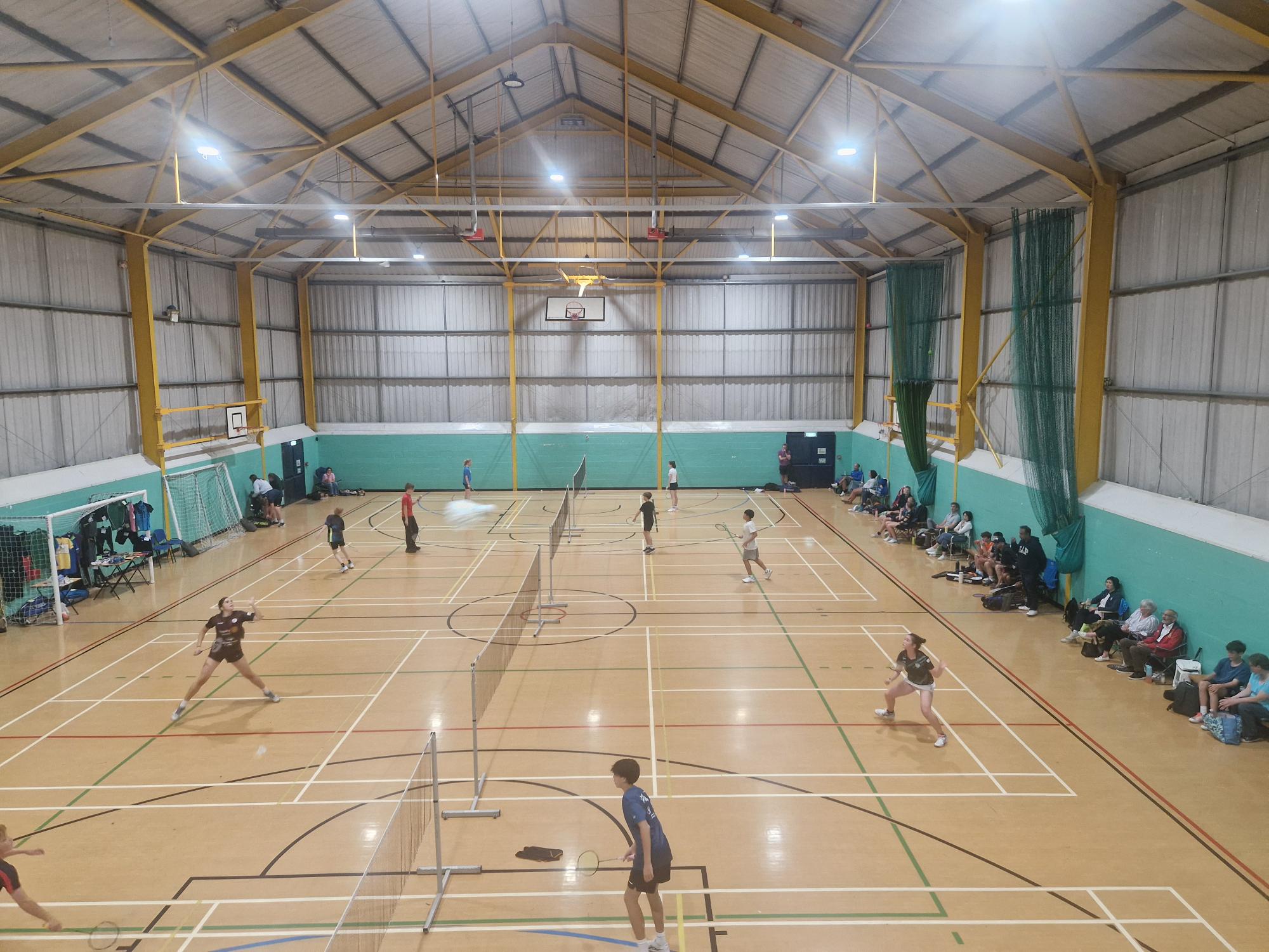 Badminton matches in progress across a sports hall at the JCB summer tournament