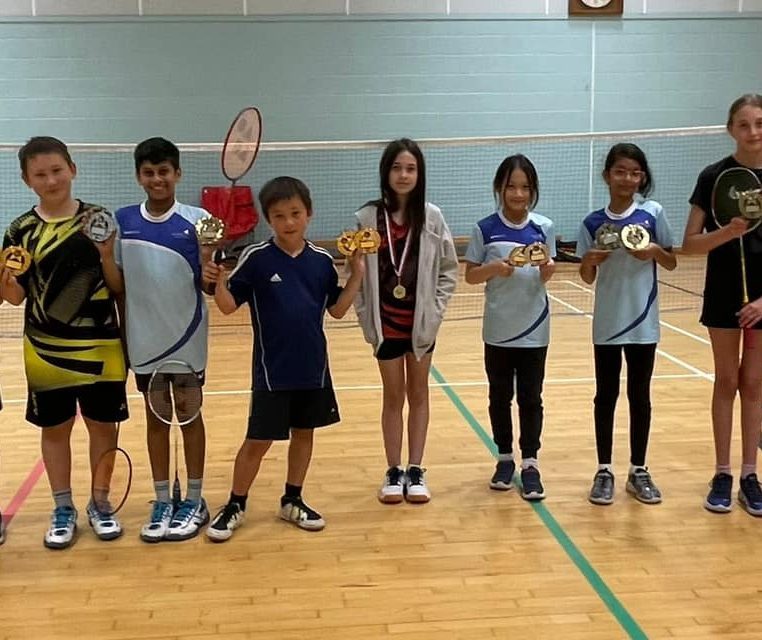 Junior badminton players with trophies and medals on court